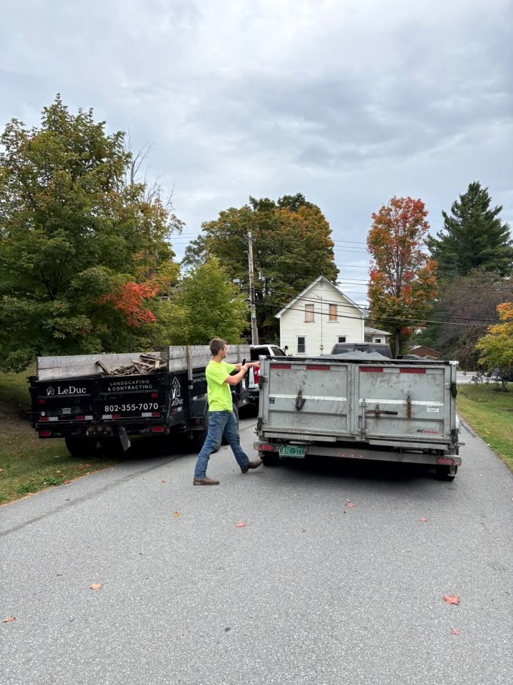 T&M Hauling crew member at a job site between a loaded dump trailer and an enclosed trailer